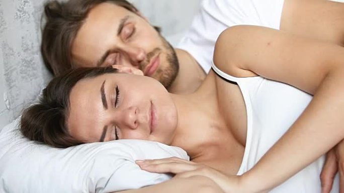 年轻夫妇睡在床上，躺在白色亚麻布上拥抱