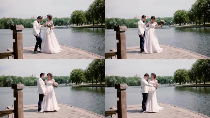 幸福的夫妇在他们的婚礼上跳舞，在码头上玩得开心。夏天公园里的河。婚礼服装