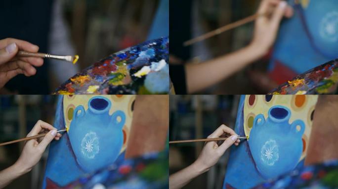 在艺术家工作室，女人的手用画笔在调色板中混合颜料和在画布上绘画静物画的特写跟踪镜头