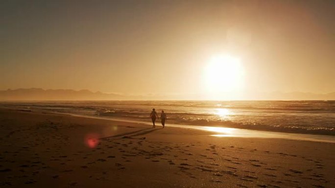 日落时分，两个剪影人物在沙滩上漫步