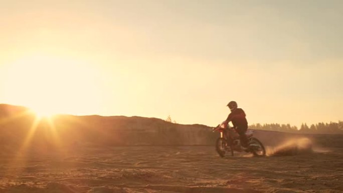 专业的摩托车越野赛车手在越野沙地上驾驶。这是日落和轨道覆盖着烟，雾和朦胧的阳光。