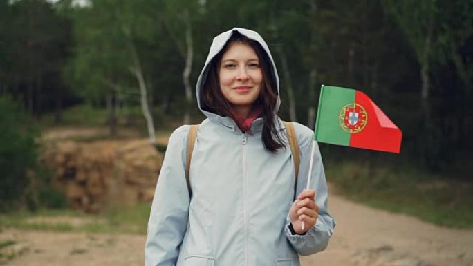 拿着葡萄牙国旗的迷人葡萄牙女孩的慢动作肖像，微笑着看着相机。公民，民族自豪感，春天的概念。