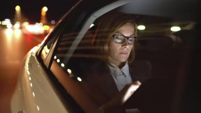 女商人女士在夜间驾驶的汽车后座上使用平板电脑