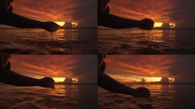 剪影: 年轻女子在美丽的夜晚用手sc起海水