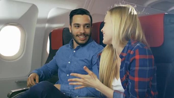 在商业飞机上，英俊的西班牙裔男子向他美丽的金发女友讲述了有趣的故事。两人都笑了。他们乘坐新飞机旅行，