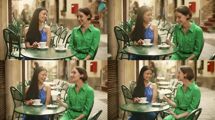 两个穿着浅色夏装的迷人年轻女性在街头咖啡店放松和交谈。女人心情很好，面带微笑。