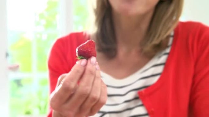 女人从碗里摘了一个新鲜的草莓，然后吃东西