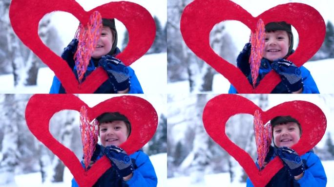 学龄前男孩的肖像通过红色的心看着相机