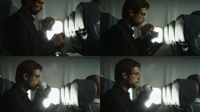 年轻人在飞机上喝咖啡，一个女人在窗户旁边的背景中看书。