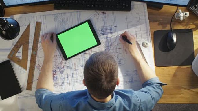 建筑工程师的俯视图借鉴了他的蓝图，与绿屏平板电脑相比，还使用台式电脑。他的桌子上摆满了有用的物品和早
