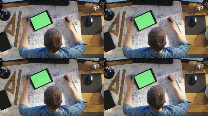 建筑工程师的俯视图借鉴了他的蓝图，与绿屏平板电脑相比，还使用台式电脑。他的桌子上摆满了有用的物品和早