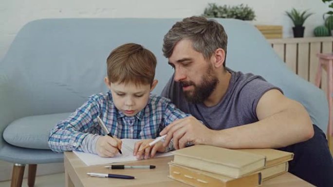 孩子正在学习，在练习本上写单词，他的父亲正在教他坐在桌子旁，向儿子解释规则。教育、童年和父亲观念。
