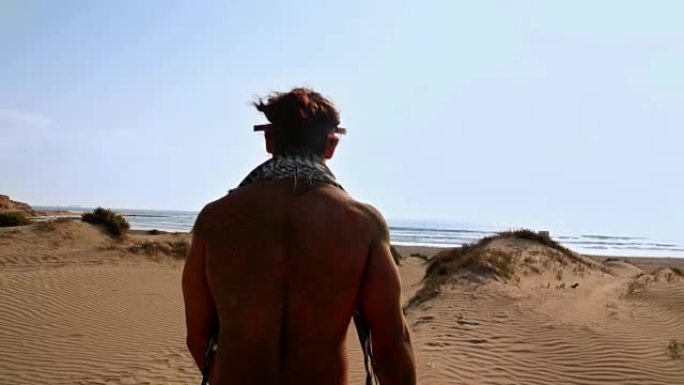 年轻的肌肉发达的男人带着蒸汽朋克护目镜走向海滩