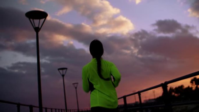 日落时跑步的年轻女性的后视图