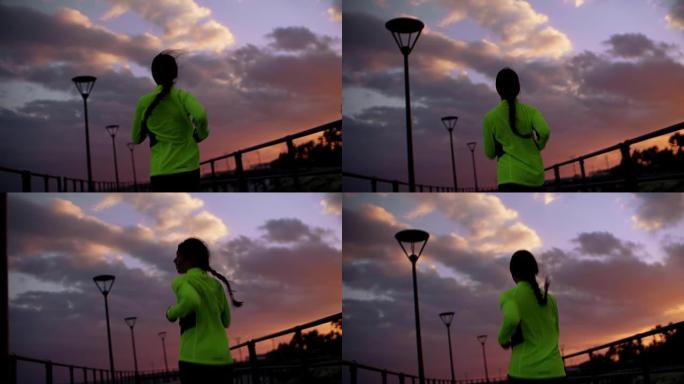 日落时跑步的年轻女性的后视图