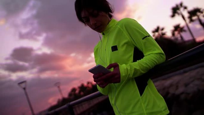 日落时穿着运动服的年轻女子在手机上发短信
