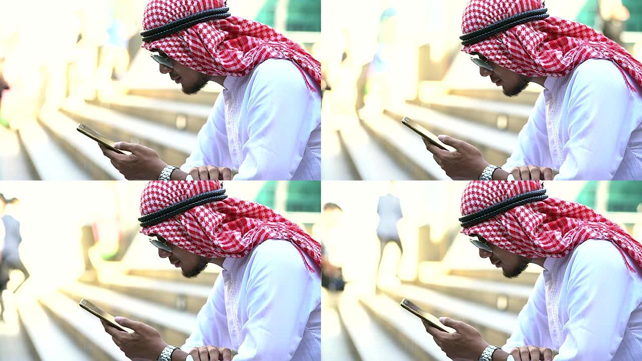 紧张的大胡子阿拉伯商人坐在户外人行道上玩手机。