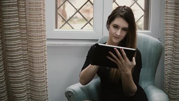 使用带触摸屏的平板电脑，坐在公寓和互联网上购物的年轻美女的肖像