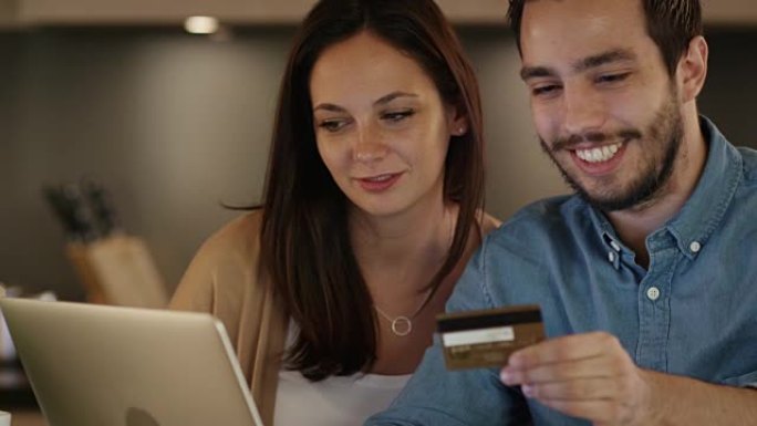 年轻夫妇使用信用卡在笔记本电脑上购买东西。