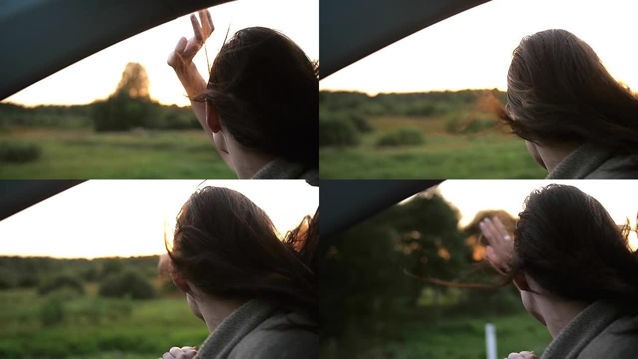 快乐的女人喜欢夏天开车旅行。通过汽车的窗户向空中传递。日落光线。慢mo