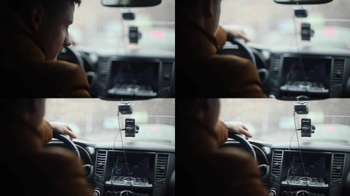 男人坐在车里，俯视。左手在方向盘上。前窗上的雨滴。后视图