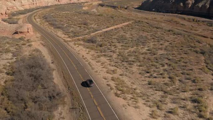 空中: 黑色SUV汽车沿着蜿蜒的空旷道路穿越峡谷谷
