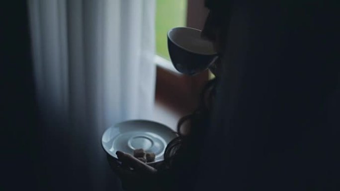 黑发女人看着远处喝茶的特写镜头。女性独自在家度过早晨