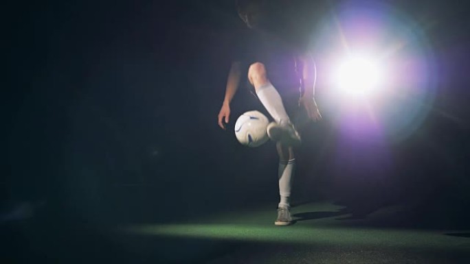 足球运动员剪影。职业足球运动员在黑暗中带球练习。