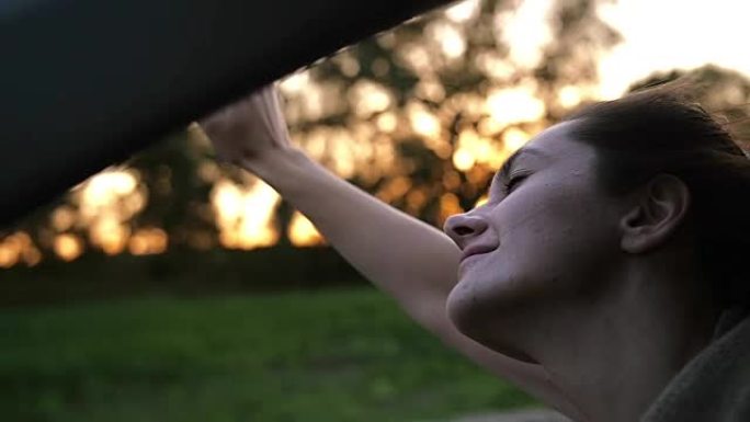 车上的漂亮女人，幸福地闭上眼睛，在空中玩耍。日落。风吹头发。慢mo