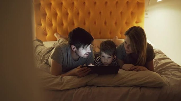幸福家庭有小儿子a躺在家里床上睡觉前用平板电脑看卡通电影