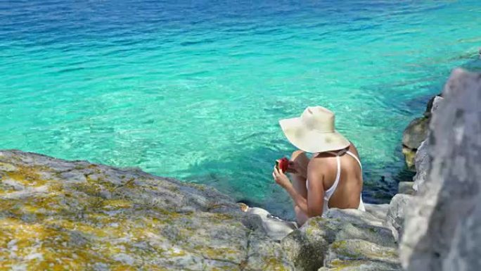 穿着泳衣和太阳帽的女人在宁静的蓝色海洋上吃新鲜的西瓜