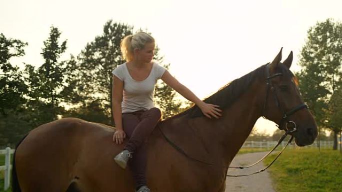 慢动作美丽的女孩在阳光明媚的早晨坐在一匹马，双腿交叉