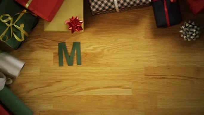 一名男子剪字母 “圣诞快乐”，并用礼品盒将其放在木桌上的俯视图延时。动态摄像机。