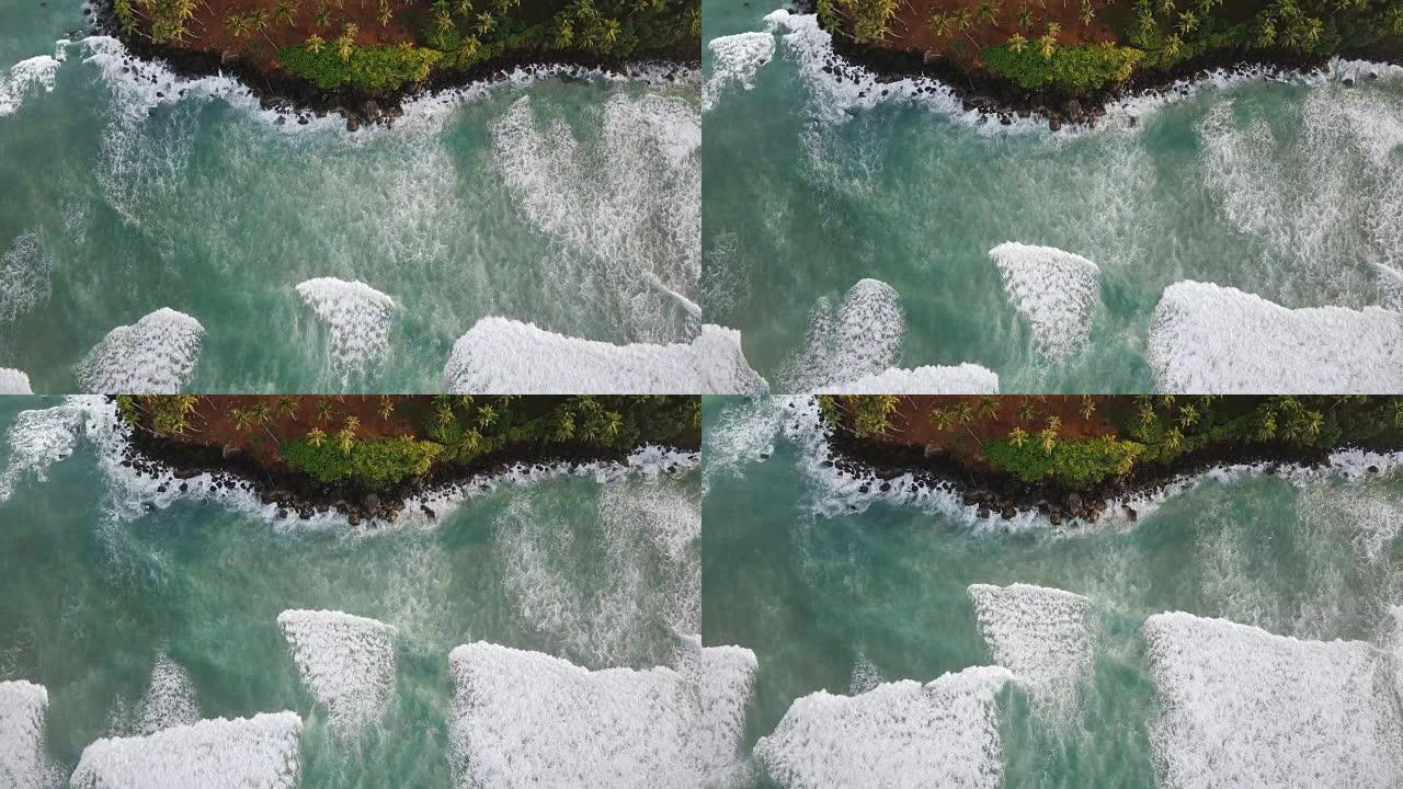 无人机俯视图锁定拍摄美丽的泡沫海浪到达风景如画的异国海岸，热带树木