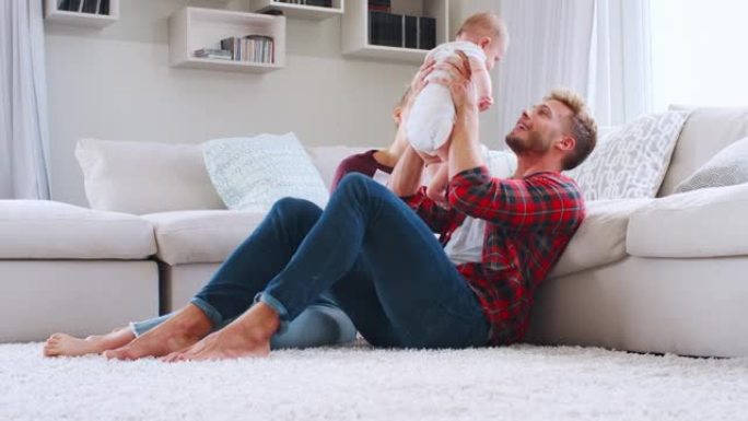 年轻的白人夫妇坐在家里举起婴儿，侧视