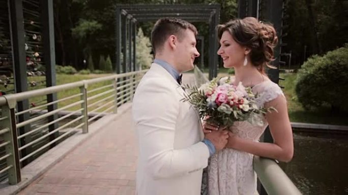 一对美丽相爱的夫妇婚礼当天的侧视图。穿着白色婚纱的新娘，在桥上穿着礼服的新郎