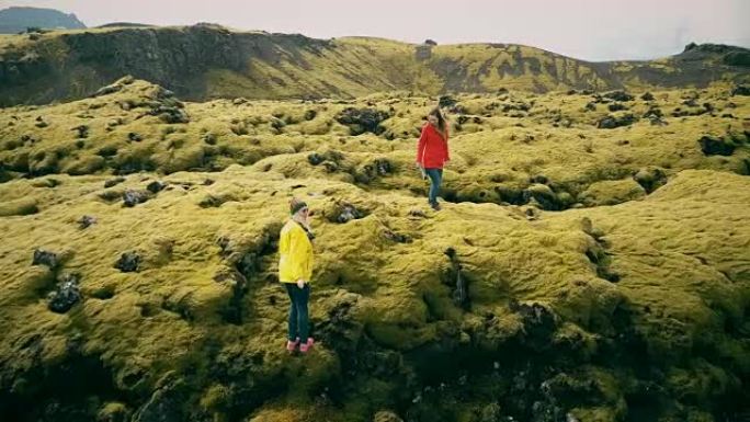 在冰岛的熔岩场上徒步旅行的两个女人的鸟瞰图。游客摔倒在柔软的苔藓上