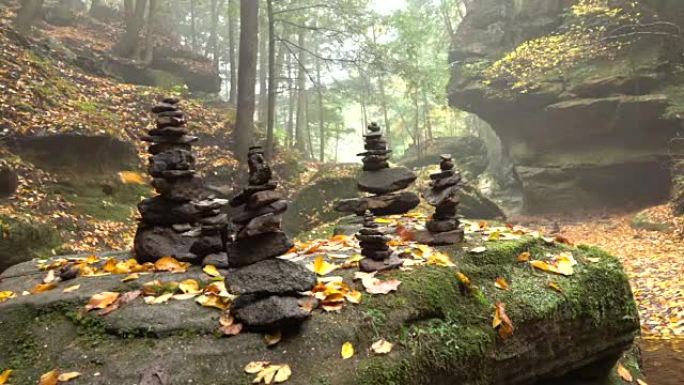 特写: 一堆堆积在岩石上的石头在华丽的雾蒙蒙的秋天云杉森林