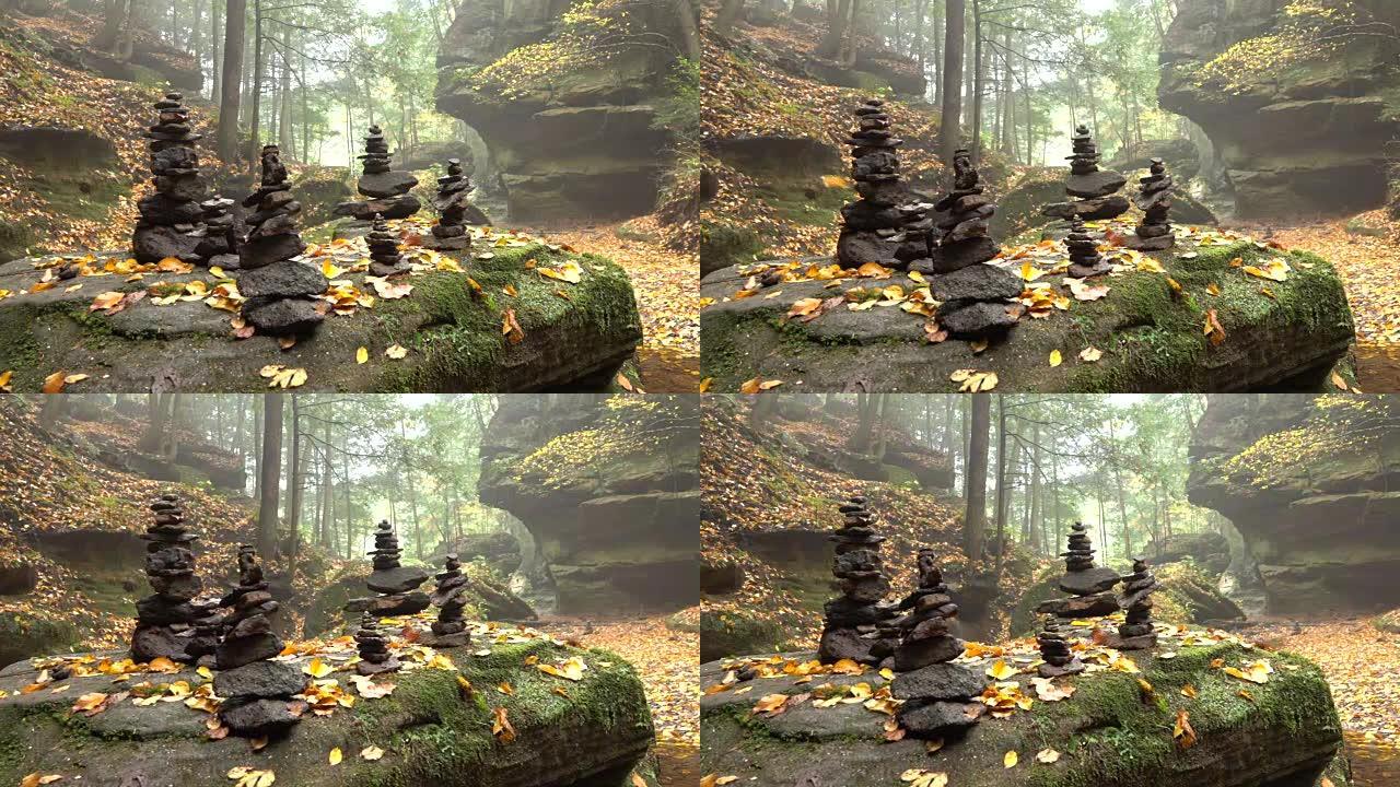 特写: 一堆堆积在岩石上的石头在华丽的雾蒙蒙的秋天云杉森林