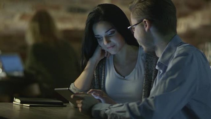 年轻夫妇晚上在咖啡店里使用平板电脑娱乐。休闲生活方式。
