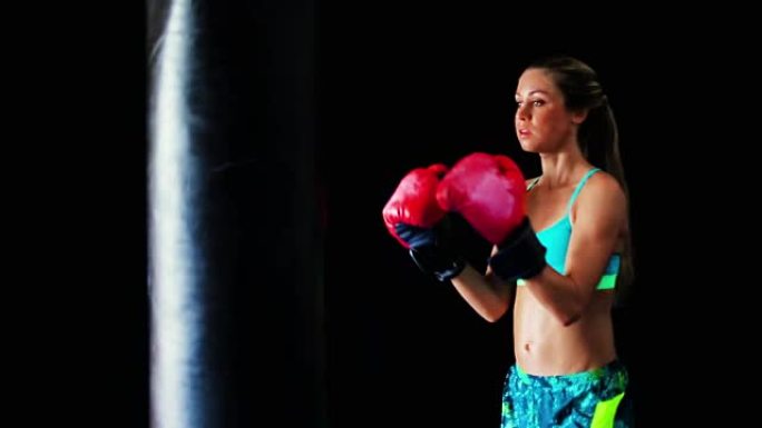 美丽的年轻女运动员锻炼自我防卫与拳击手套和身体袋。