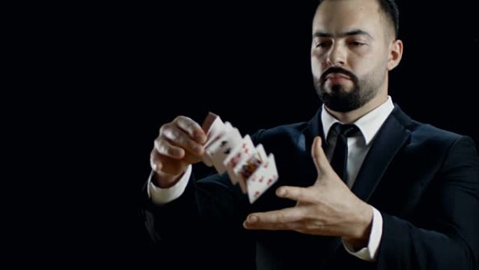穿着黑色西装表演纸牌把戏的专业魔术师的特写镜头。在空中投掷和捕捉纸牌。背景是黑色的。慢动作。