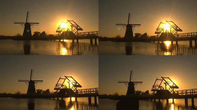 日落时以传统风车为背景的河上木制吊桥