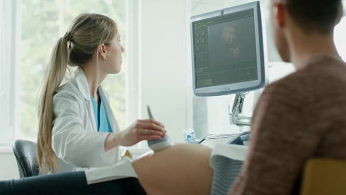 在医院，孕妇躺在床上，产科医生按下控制面板上的按钮并开始超声/超声检查程序。丈夫支持他的妻子。