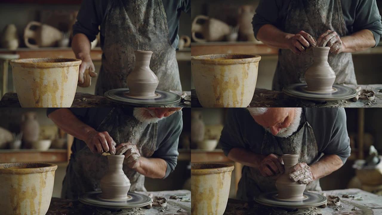 老年工匠正在使用专业工具在陶工轮上制作陶瓷罐。工作场所有手工制作的罐子，漂亮的花瓶和背景人物。