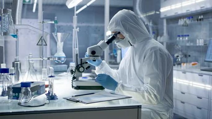 在安全的高水平研究实验室中，Coverall的科学家在显微镜下检查培养皿。