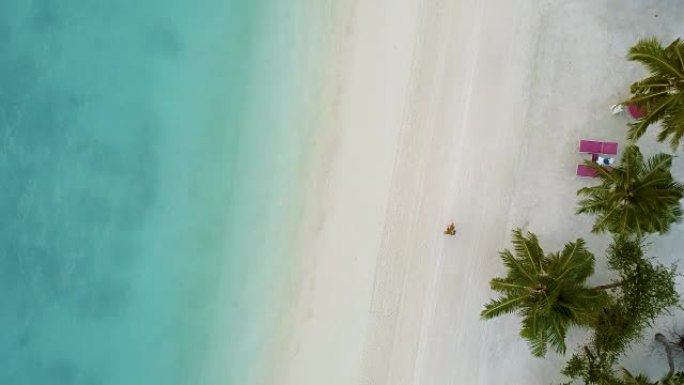 女人在海滩上漫步的俯视图。美丽的沙滩是白色的，平静的大海是海蓝宝石或绿松石。