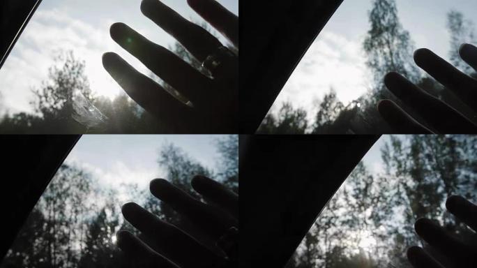 在旅途中，车窗上有戒指的手的特写。阳光透过手指和树木。手指手掌。慢mo