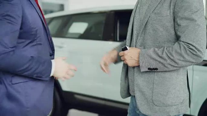 汽车陈列室的男工人正在将车钥匙交给买家年轻人，并与他站在豪华新车旁边握手。买卖车辆概念。