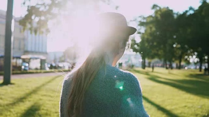 日落时，戴着帽子的年轻美女在公园散步，使用智能手机，在触摸屏上打字